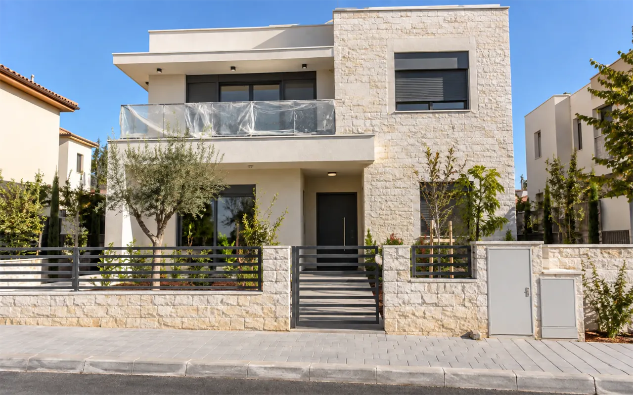 תמונה להמחשה: בית פרטי חדש בשתי קומות שהבנייה בו הסתיימה: חזית טיח וחיפוי אבן בהיר, חלונות אלומיניום עם תריסים, שביל כניסה ושער מתכת, ארונות מונים בגדר וניילון מגן שנשאר על מעקה המרפסת